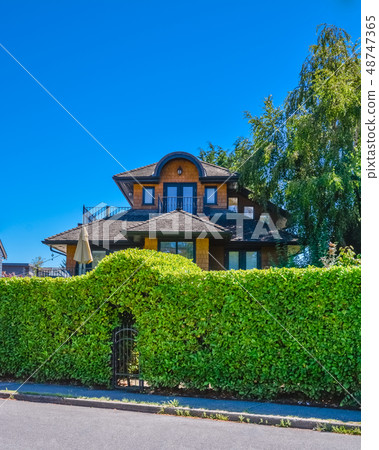 Green hedge with arch over entrance gate in front of residential house. 48747365