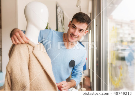 Young man putting clothes on a mannequin in store. Young man putting clothes on a mannequin in store. 48749213