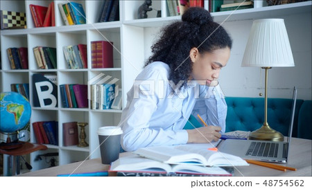 Female student making a note while preparing for exams in university library. Young african american Female student making a note while preparing for exams in university library. Young african american 48754562