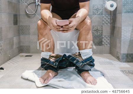Man using the smart mobile phone when sitting on toilet bowl 48756645