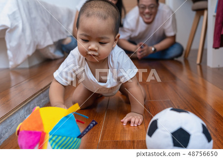 Asian baby boy crawl and playing the ball on the wooden floor over the photo blurred of father and mother cheering up in the bedroom,Family Lifestyle Concept Asian baby boy crawl and playing the ball on the wooden floor over the photo blurred of father and mother cheering up in the bedroom,Family Lifestyle Concept 48756650
