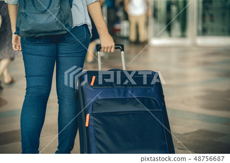 Closeup hand holding the luggage over the flight board for check-in at the flight information screen in modern an airport, travel and transportation concept 48756687