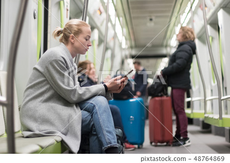 Beautiful blonde woman wearing winter coat reading on the phone while traveling by metro public 48764869
