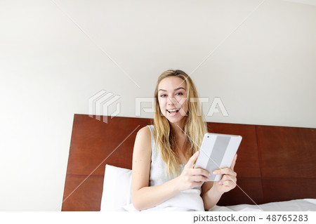 portrait of super happy young woman hold tablet at white bed 48765283