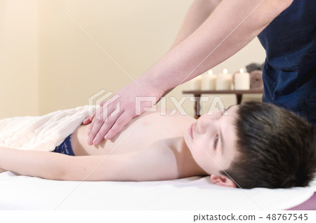 A little boy at the reception at a professional masseuse. Male manual worker gives massage to the A little boy at the reception at a professional masseuse. Male manual worker gives massage to the 48767545