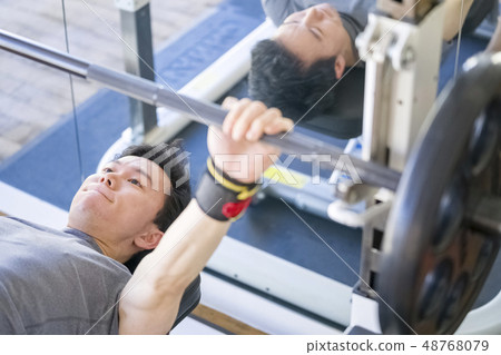 Stoic young male thin macho doing bench press with serious look at training gym Stoic young male thin macho doing bench press with serious look at training gym 48768079
