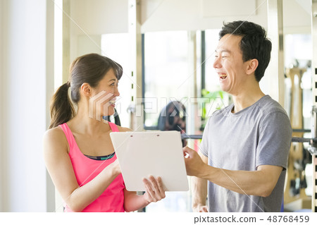 Young male office worker fine macho receiving explanation of muscle training from beauty instructor at personal gym 48768459