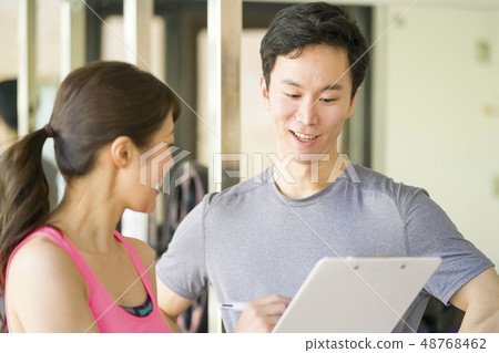 Young male office worker fine macho receiving explanation of muscle training from beauty instructor at personal gym Young male office worker fine macho receiving explanation of muscle training from beauty instructor at personal gym 48768462