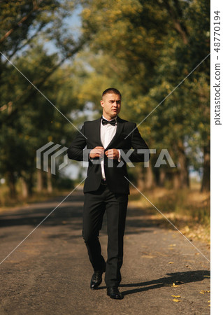 Young groom in suit otside. Handsome man in black suit. Model walking in the park Young groom in suit otside. Handsome man in black suit. Model walking in the park 48770194