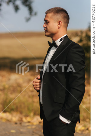 Young groom in suit otside. Handsome man in black suit. Model walking in the park Young groom in suit otside. Handsome man in black suit. Model walking in the park 48770218
