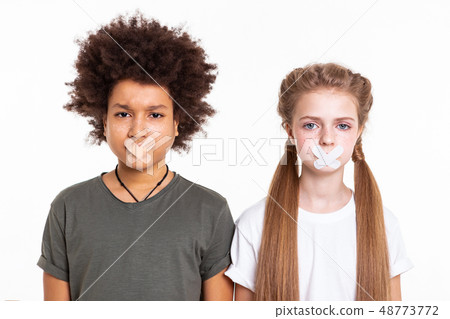 Scared confused young kids standing with taped mouths Scared confused young kids standing with taped mouths 48773772