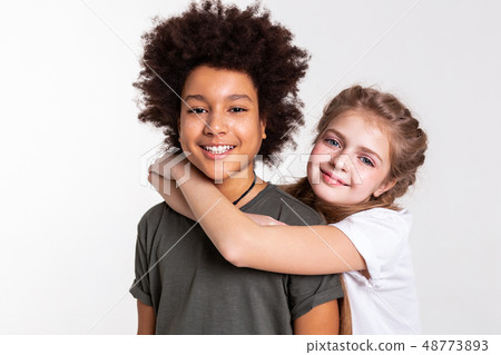 Smiling light-haired girl hanging on her African American boy Smiling light-haired girl hanging on her African American boy 48773893