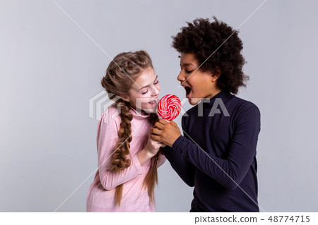 Active beaming opposite kids biting one candy together 48774715