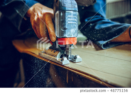Carpenter using circular saw for cutting wooden boards. 48775156