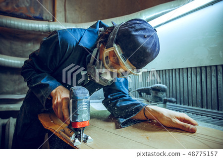 Carpenter using circular saw for cutting wooden boards. 48775157