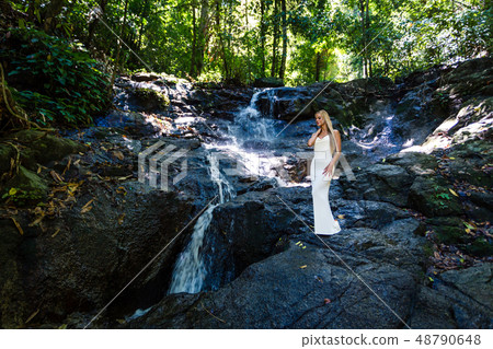 Young woman in white dress is posing at waterfall 48790648