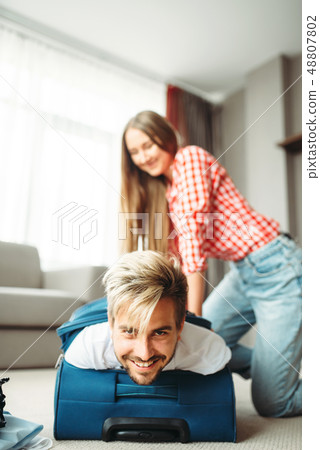 Cheerful girl packed her husband in a suitcase Cheerful girl packed her husband in a suitcase 48807802