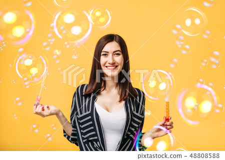 Young woman blows soap bubble, yellow background Young woman blows soap bubble, yellow background 48808588