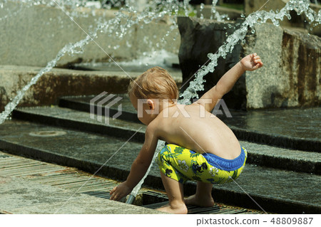 Funny baby boy trying to cauch water stream in fountain. Cute toddler playing in the city fountain Funny baby boy trying to cauch water stream in fountain. Cute toddler playing in the city fountain 48809887