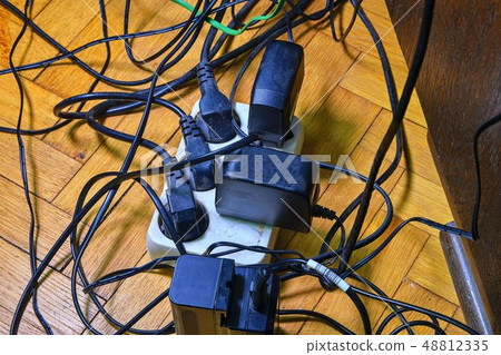 Tangled wires and battery charges on parquete floor. Domestic appliances. Wires mess in domestic 48812335