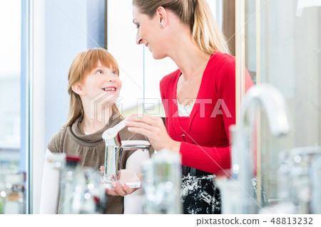 Happy mother looking with her daughter at two faucets in a sanitary ware shop 48813232