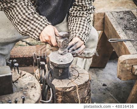 Blacksmith hand with a hammer on steel anvil . Hand of a blacksmith with hammer close up. The Blacksmith hand with a hammer on steel anvil . Hand of a blacksmith with hammer close up. The 48816416