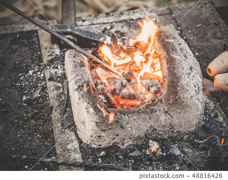 The blacksmith holds the billet over hot coals in a clay oven. blacksmith heating iron metal sword 48816426