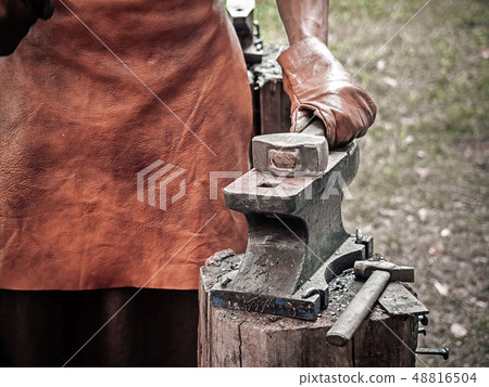 . Blacksmith hand with a hammer on steel anvil . Hand of a blacksmith in leather gloves with hammer . Blacksmith hand with a hammer on steel anvil . Hand of a blacksmith in leather gloves with hammer 48816504
