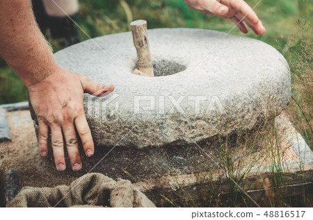 The ancient quern stone hand mill with grain. The man grinds the grain into flour with the help of a 48816517