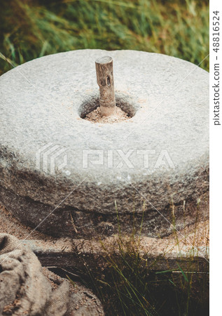 The ancient stone hand mill with grain. Medieval hand-driven millstone grinding wheat. Old quern 48816524