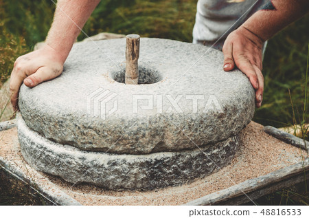 The ancient quern stone hand mill with grain. The man grinds the grain into flour with the help of a 48816533