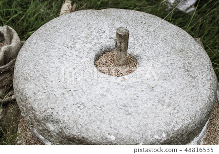 The ancient stone hand mill with grain. Medieval hand-driven millstone grinding wheat. Old quern 48816535