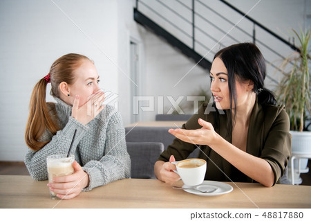 Two young women argue in cafe while drinking coffee Two young women argue in cafe while drinking coffee 48817880