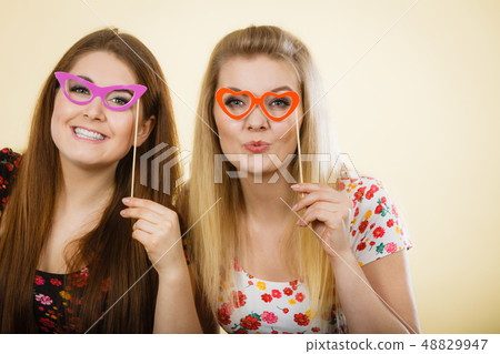 Two happy women holding fake eyeglasses on stick Two happy women holding fake eyeglasses on stick 48829947
