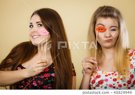 Two happy women holding fake lips on stick Two happy women holding fake lips on stick 48829949
