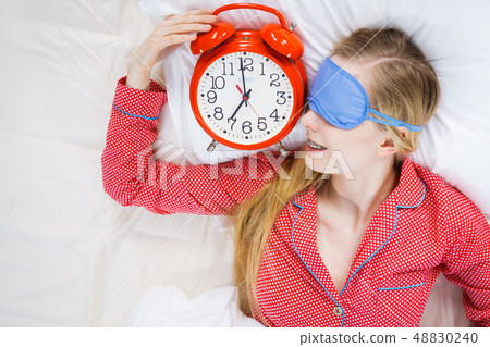 Sleeping woman wearing pajamas holding clock 48830240