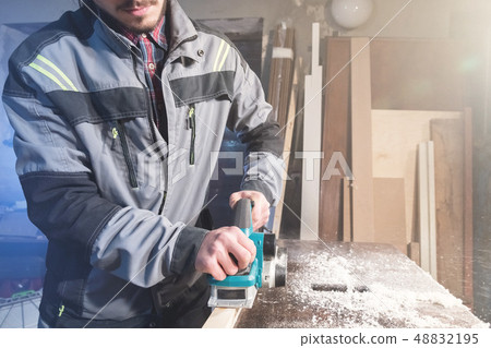 Young carpenter with a beard working with an electric plane with suction of sawdust. Leveling and 48832195