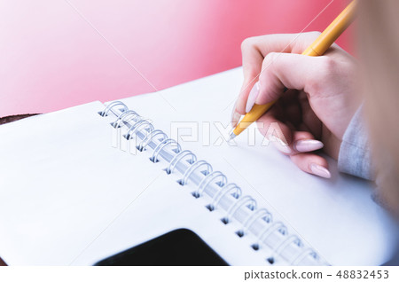 Close-up from behind the back of a young woman in a winter polto is holding a ballpoint pen and is Close-up from behind the back of a young woman in a winter polto is holding a ballpoint pen and is 48832453