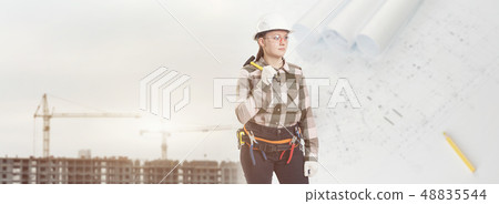 A female construction worker in safety helmet holds a hammer 48835544