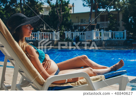 pregnant woman sunbathing on a lounger by the pool 48840627
