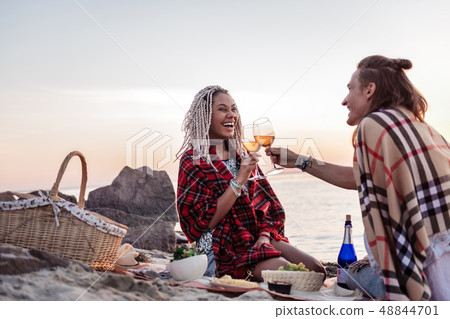 Young couple with plaids on shoulders having romantic dinner on the beach Young couple with plaids on shoulders having romantic dinner on the beach 48844701
