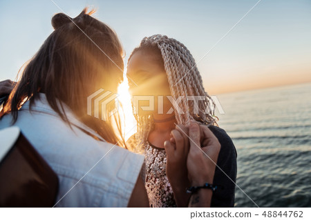 Man with long blonde hair kissing his stylish girlfriend watching the sunset Man with long blonde hair kissing his stylish girlfriend watching the sunset 48844762