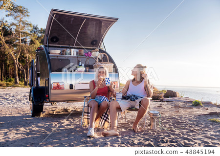 Couple sitting on chairs and eating croissants near mobile home 48845194