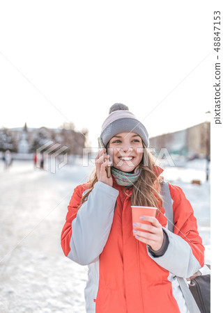 A girl with a phone is standing in winter in city, happy is laughing and talking on smartphone with A girl with a phone is standing in winter in city, happy is laughing and talking on smartphone with 48847153