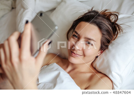 Beautiful girl lying on the bed, smiling and looking into the phone Beautiful girl lying on the bed, smiling and looking into the phone 48847604