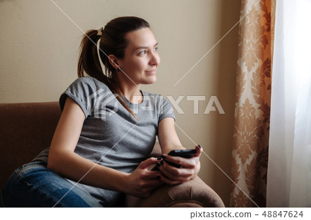 The girl sits on an armchair in a hotel room and looks into the window 48847624