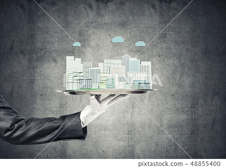 Hand holding metal tray with modern city model against concrete background Hand holding metal tray with modern city model against concrete background 48855400