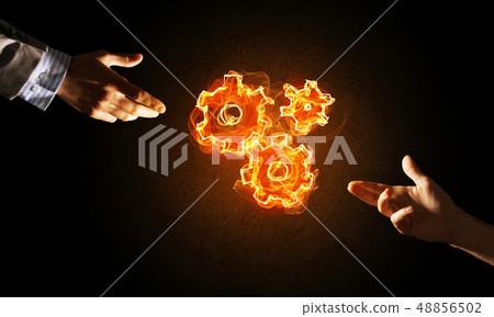 Concept of teamworking or organization presented by hands in touch and fire glowing cogwheels 48856502