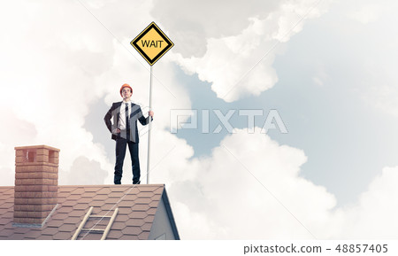 Young businessman on house brick roof holding yellow signboard. Young businessman on house brick roof holding yellow signboard. 48857405