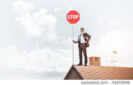 Caucasian businessman on brick house roof showing stop road sign Caucasian businessman on brick house roof showing stop road sign 48858896